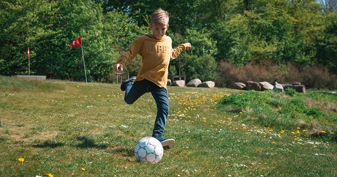 Ett barn spelar fotbollsgolf ute i naturen.