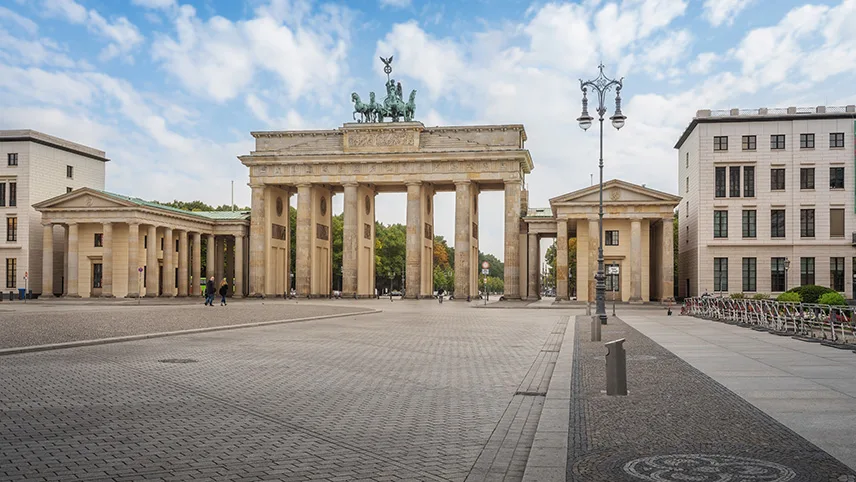 Stadsporten Brandenburger Tor sedd snett framifrån. I förgrunden syns den stora platsen framför samt ett par personer som går runt.