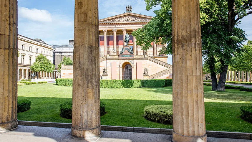 Konstmuseet Alte Nationalgalerie sett utifrån, med vackra statyer och en lummig park runt.