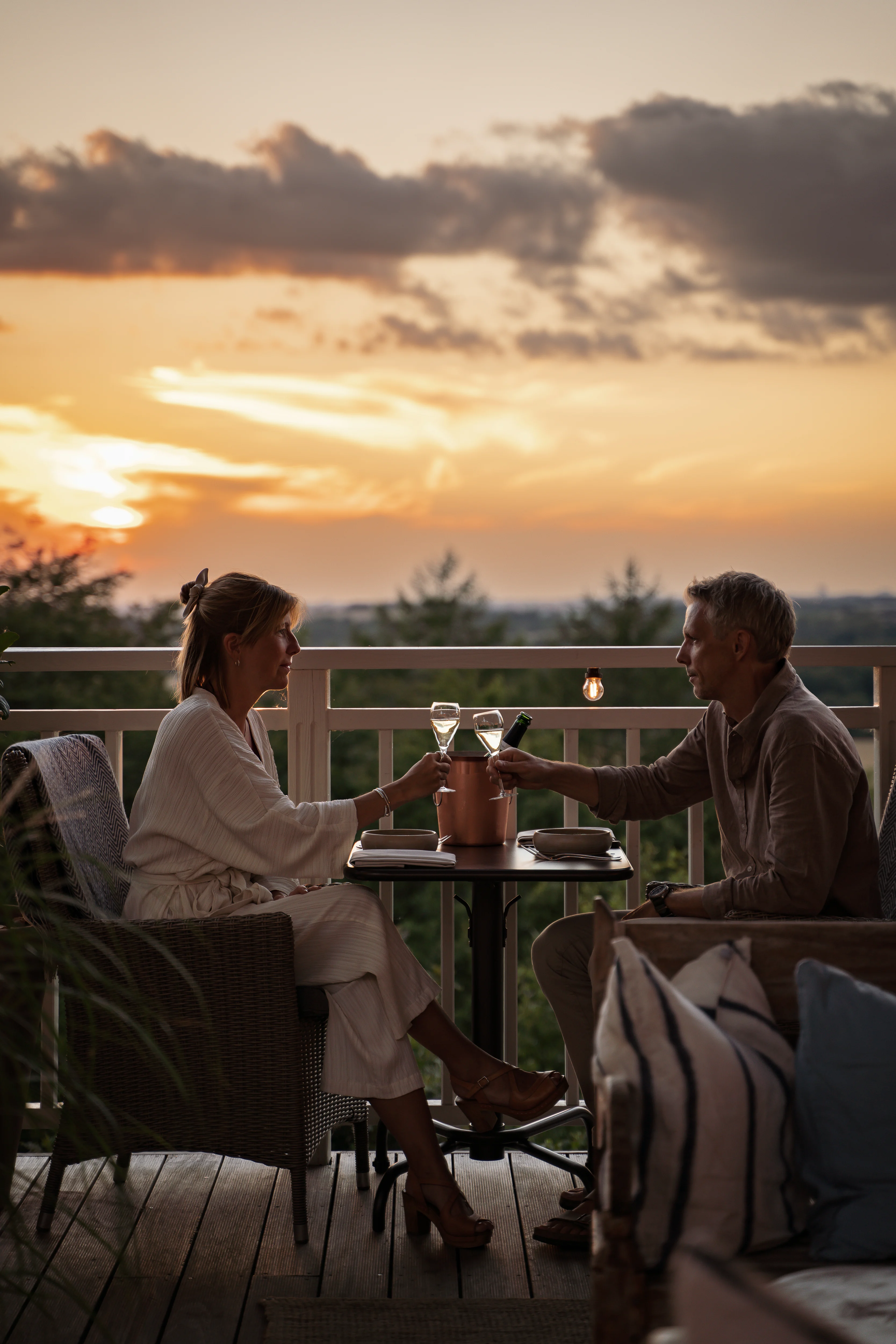 Et par drikker bobler på terrassen hos The Lodge ved solnedgang.