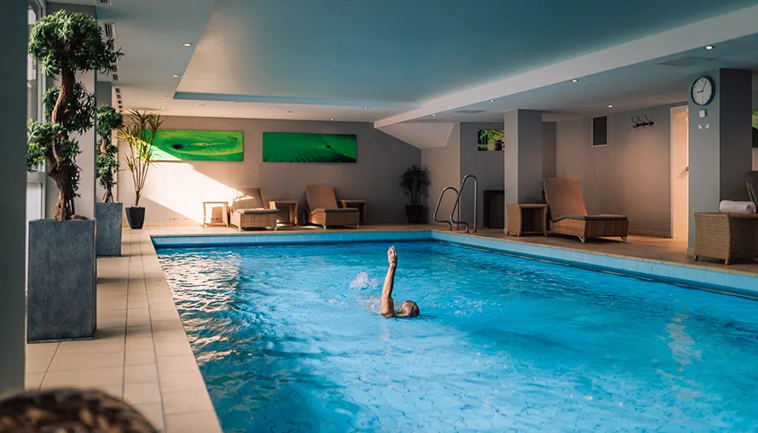 Hotellets spaavdelning med stor swimmingpool. En gäst simmar på rygg i poolen.