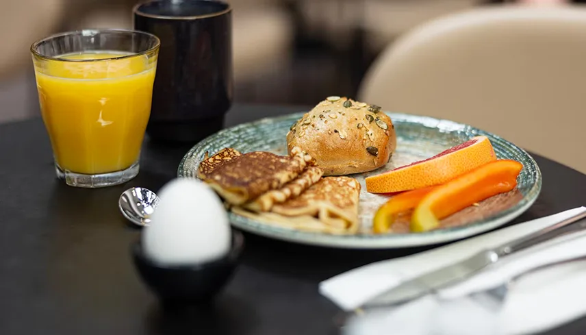 En tallrik med pannkakor, fralla och frukt samt en kopp kaffe och ett glas apelsinjuice vid hotellets frukost.