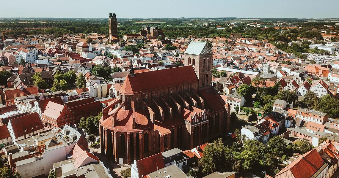 Flygfoto över en hansastad med en stor, historisk kyrka i centrum omgiven av röda tak och tät bebyggelse