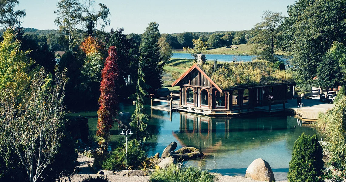 Hotelværelser på Ästad Vingård i form af en lille hytte ved vandet med træer ved siden af. 