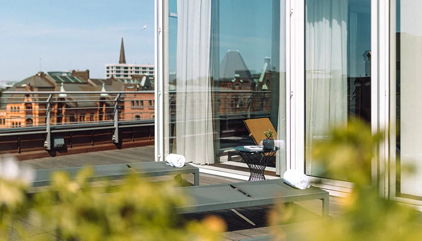 Hotellets takterrass med solsängar och gröna växter samt utsikt över staden.