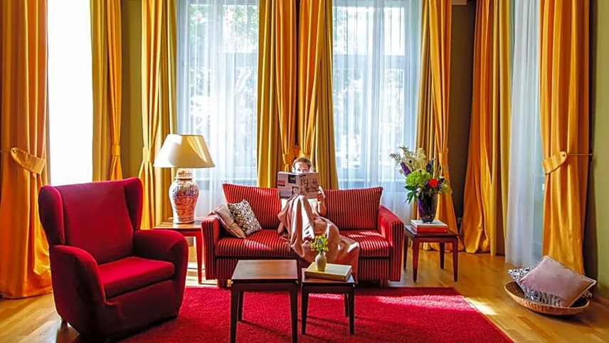 Bild från Hotel Louisa's Place med röda möbler, röd matta och långa gula gardiner. En kvinna sitter i en soffa och läser en tidning.