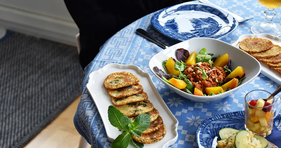 Bord med blå dug og mad serveret i form af salat og pandekager.