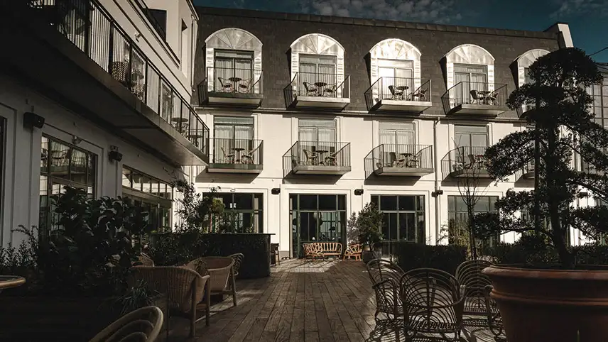 Hotellets fasad sedd mot en blå himmel med tunna slöjmoln. Fasaden är vitputsad och har stora fönster samt balkonger med möbler.