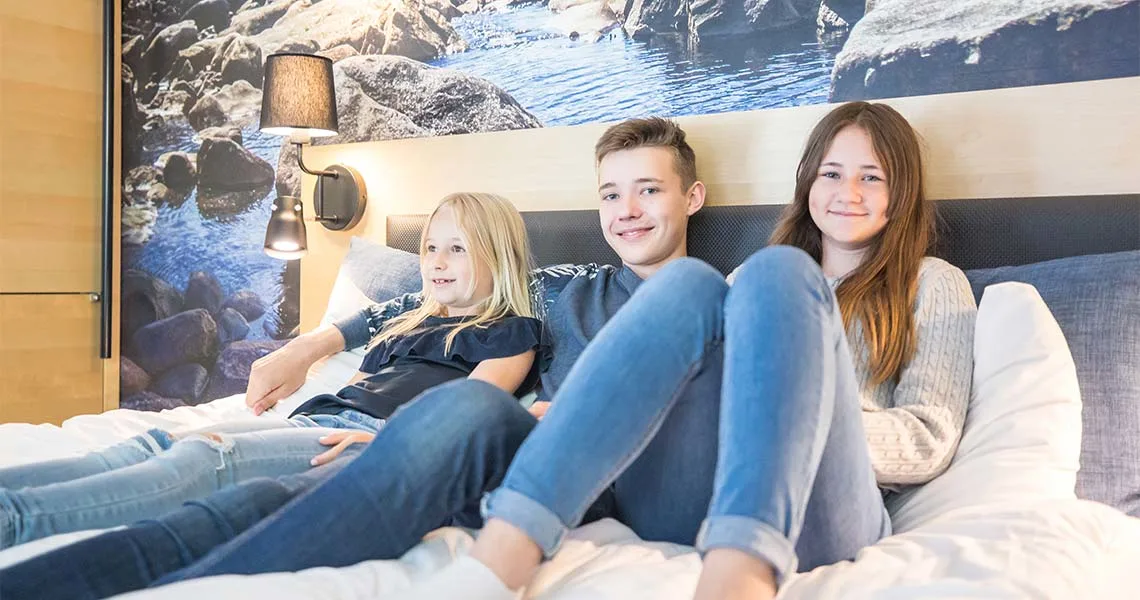 Tre børn sidder i en seng i en lejlighed på Gekås Ullared.