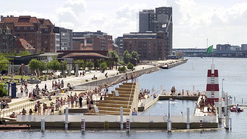 Hamnbadet Islands Brygge en vacker sommardag. Människor står på bryggan, simmar i vattnet och njuter av solen.