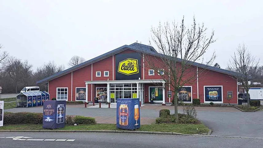 Calle Heiligenhafen sett från vägen. En röd byggnad med stor gulsvart skylt över entrén, reklam i fönstren samt en parkeringsplats utanför.
