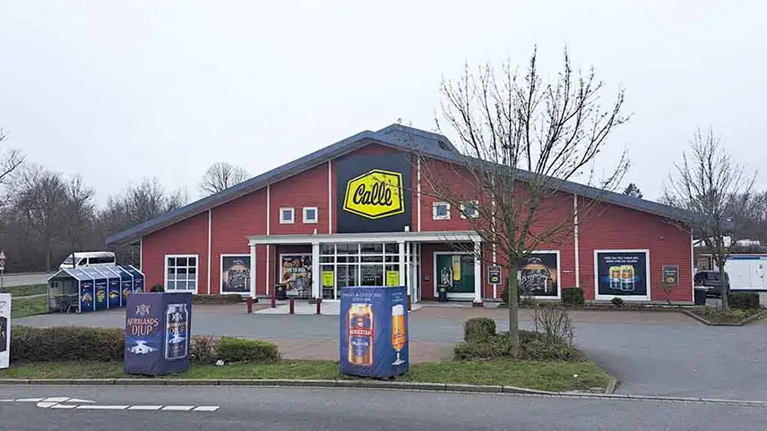 Calle Heiligenhafen sett från vägen. En röd byggnad med stor gulsvart skylt över entrén, reklam i fönstren samt en parkeringsplats utanför.