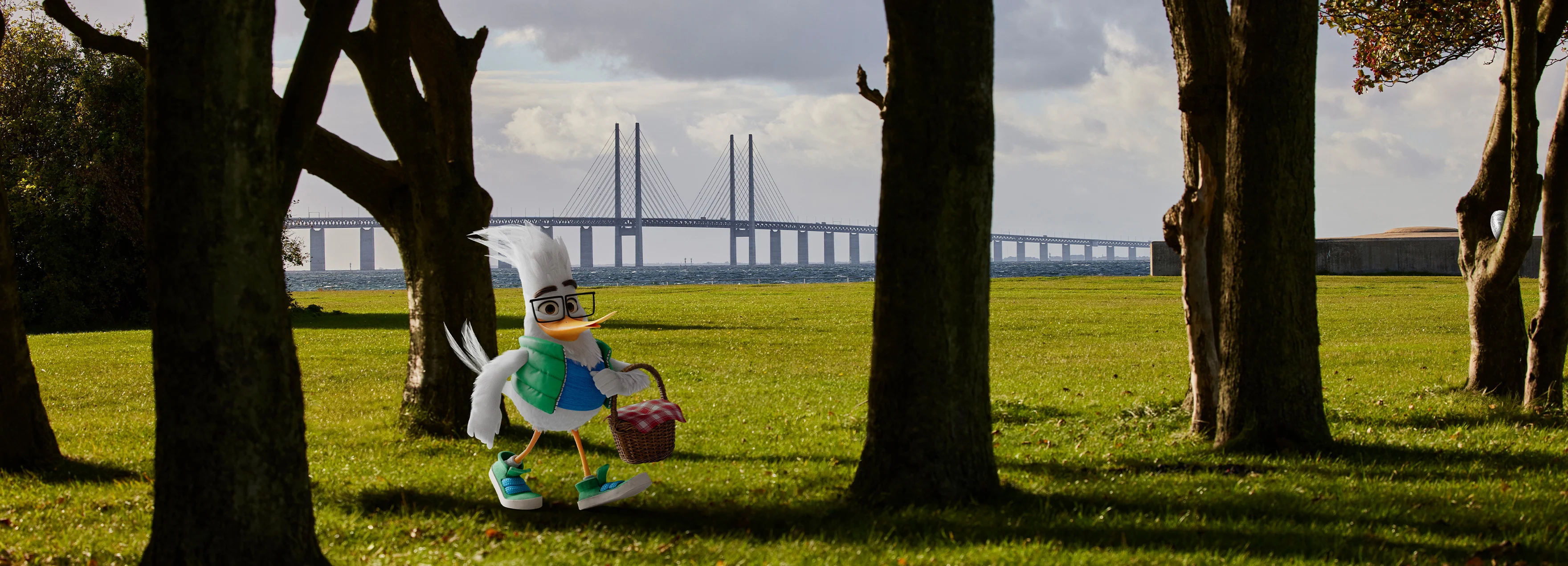 ØresundGO-maskoten Gustav går med en korg med påskägg i handen. I bakgrunden syns Öresundsbron.