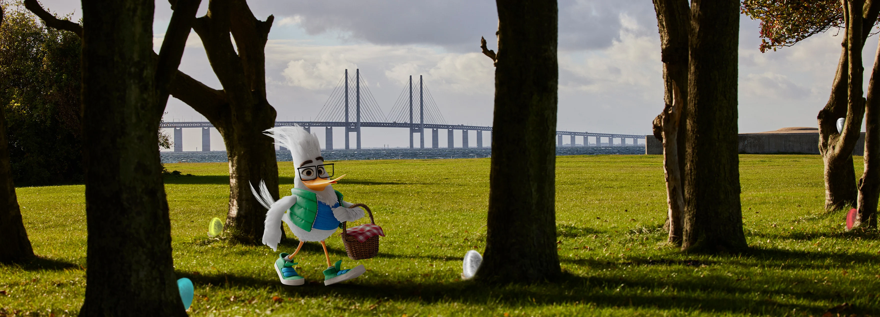 ØresundGO-maskoten Gustav går med en korg med påskägg i handen. I bakgrunden syns Öresundsbron.