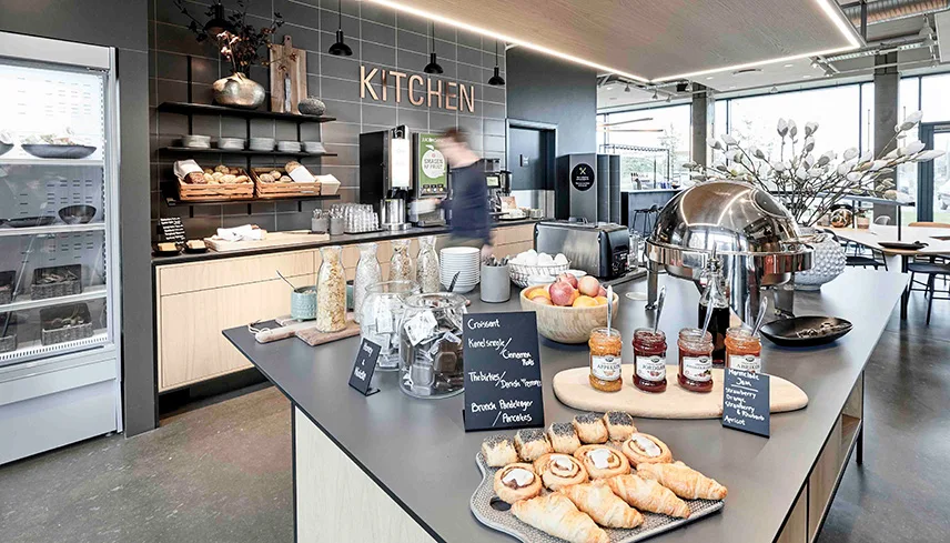 Bild från frukostbuffén. Maten står uppdukad på en stor köksö och man ser croissanter, wienerbröd, frukt, kannor med yoghurt, mjölk och juice samt en fruktskål.