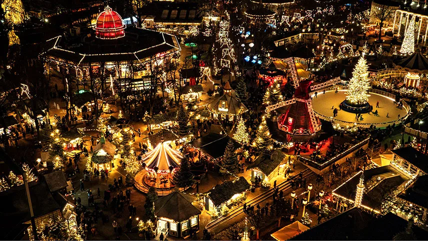 Översiktsbild tagen uppifrån av ett upplyst och julpyntat Tivoli i mörkret.