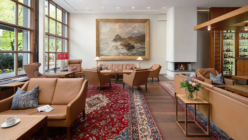 Bild från hotellets lobby med sittgrupper i ljusbrunt skinn, äkta mattor på väggarna och en öppen spis med en tänd brasa.