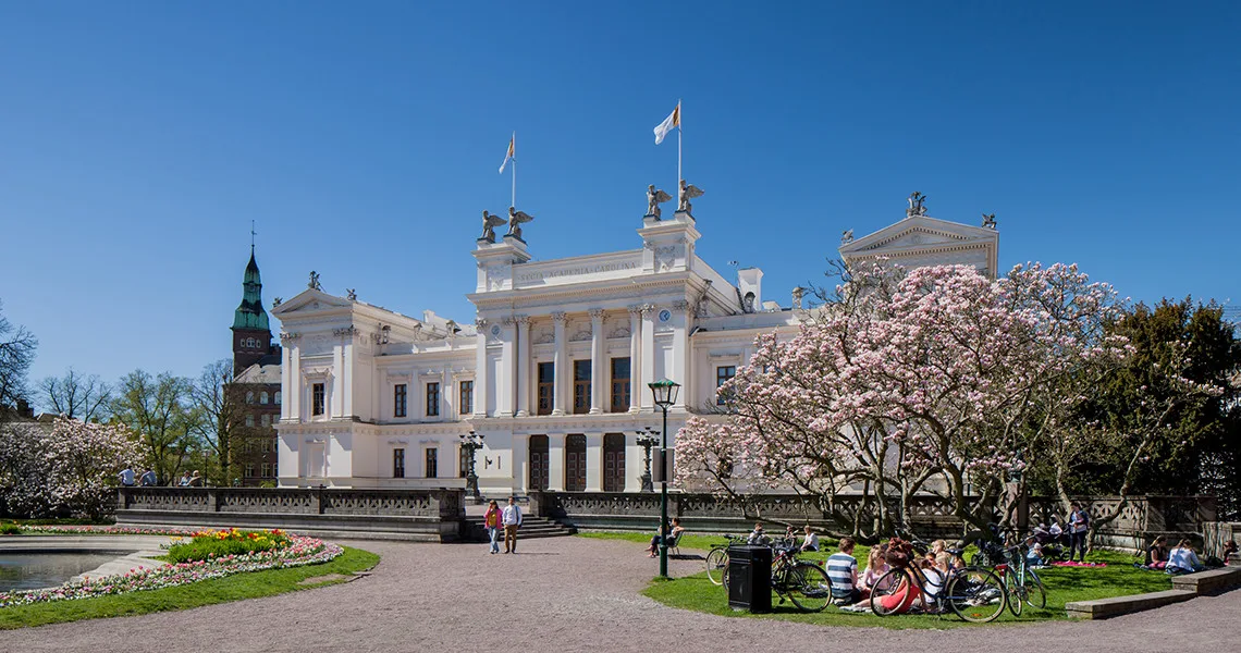 Universitetshuset i Lund med kirsebærtræer og folk, der holder picnic.