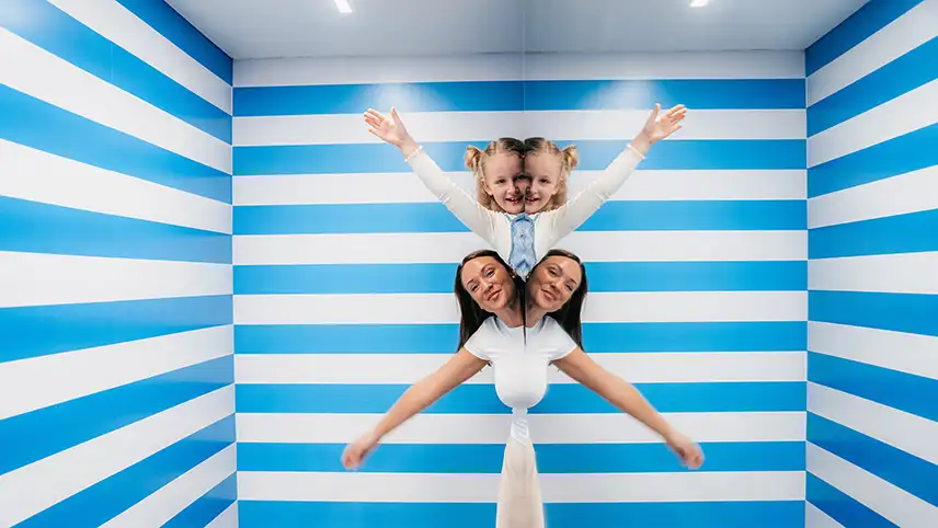 En kvinna och ett barn står i ett rum med blå- och vitrandiga väggar. Illusionen får det att se ut som att de har två huvuden var.