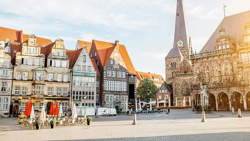 Torget i centrala Bremen med kyrkan i bakgrunden samt vackra gamla stenhus och en uteservering med stolar, bord och parasoll.