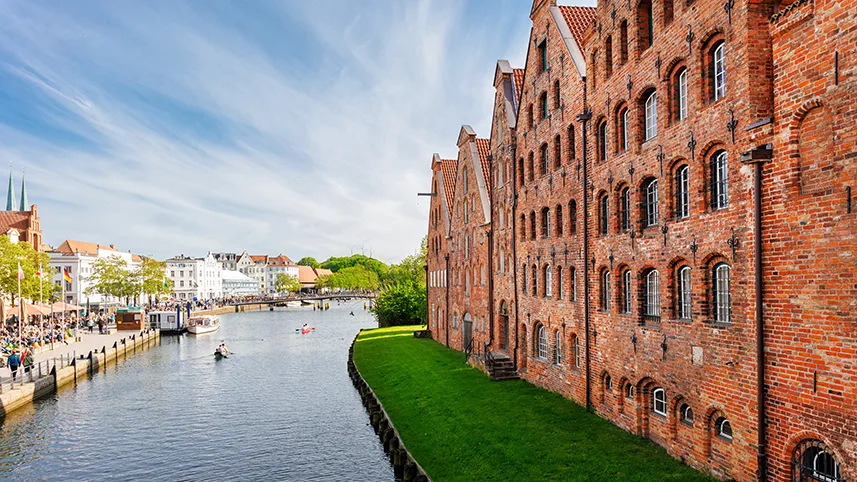 Floden Trave som rinner genom Lübeck, sedd mot grönt gräs och tegelfasader.