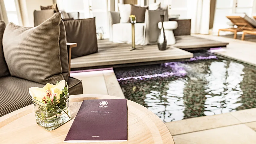 Hotellets spa med inomhuspool, loungemöbler och vackra blommor på borden.