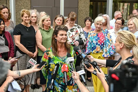 A woman standing outside of court, facing a number of journalists microphones ready to answer questions.