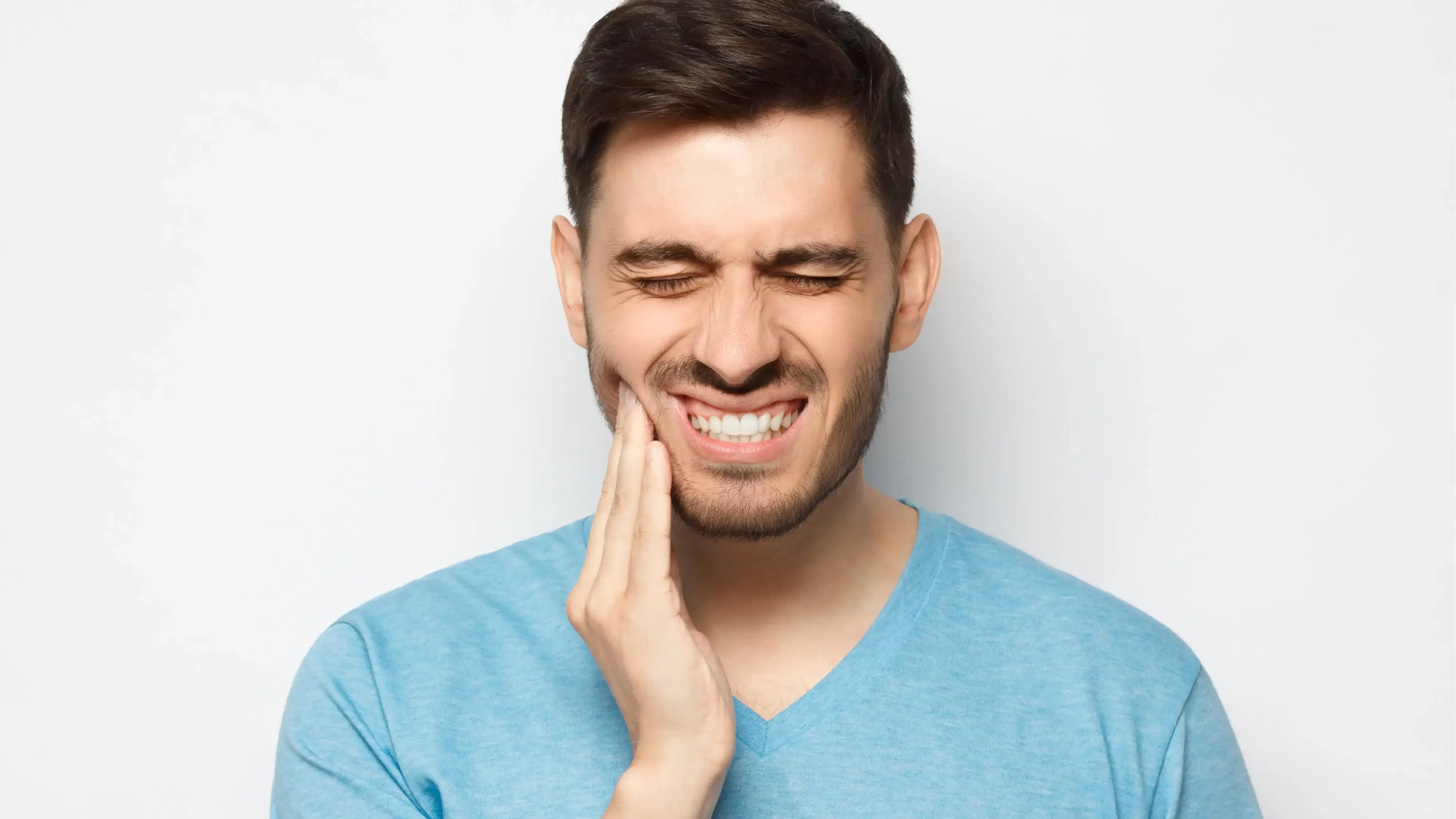 Ein jüngerer Mann, der sich schmerzvoll an seine rechte, untere Kieferseite fasst.