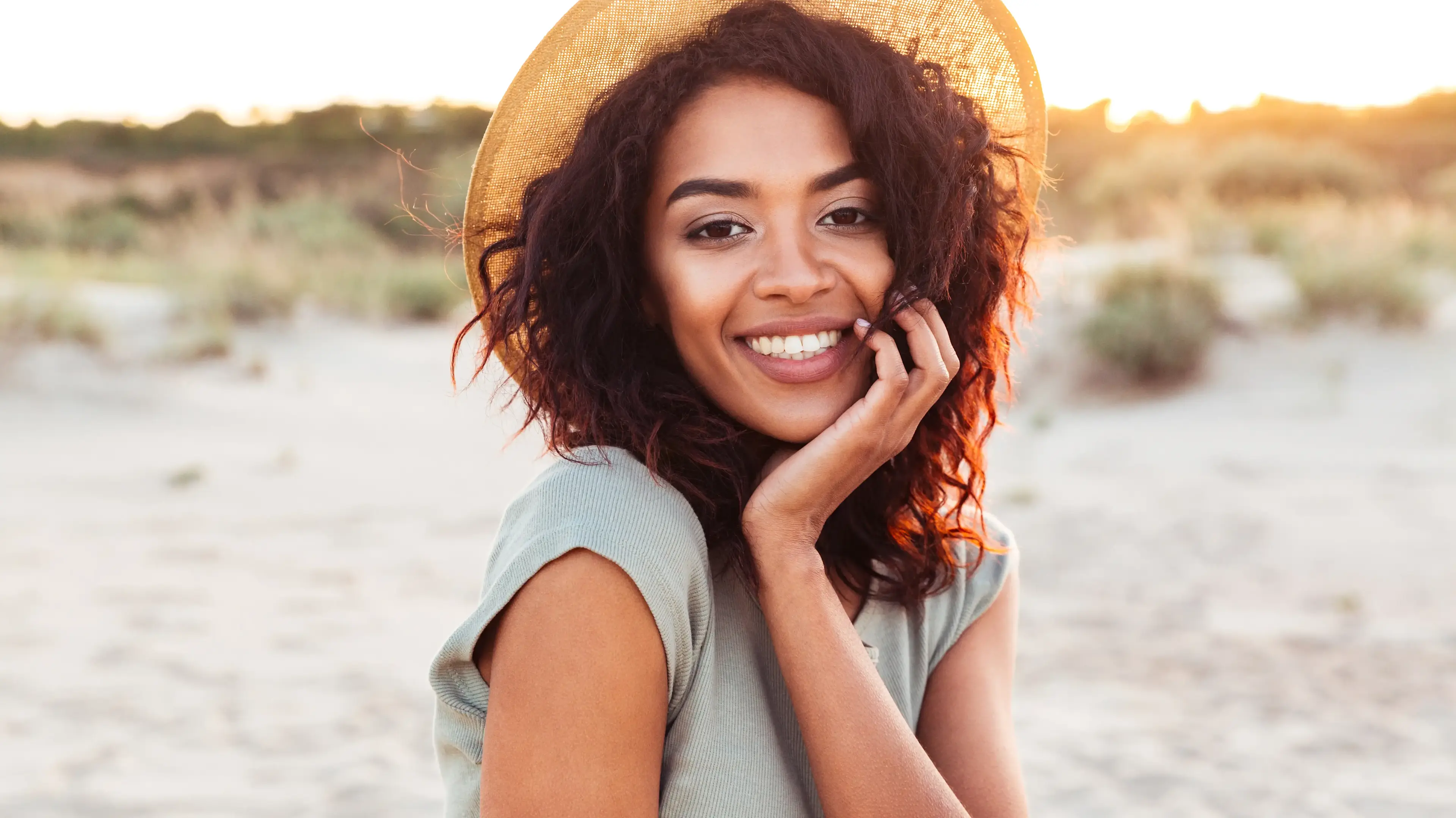 Eine lächelnde Frau am Strand mit Hut auf dem Kopf
