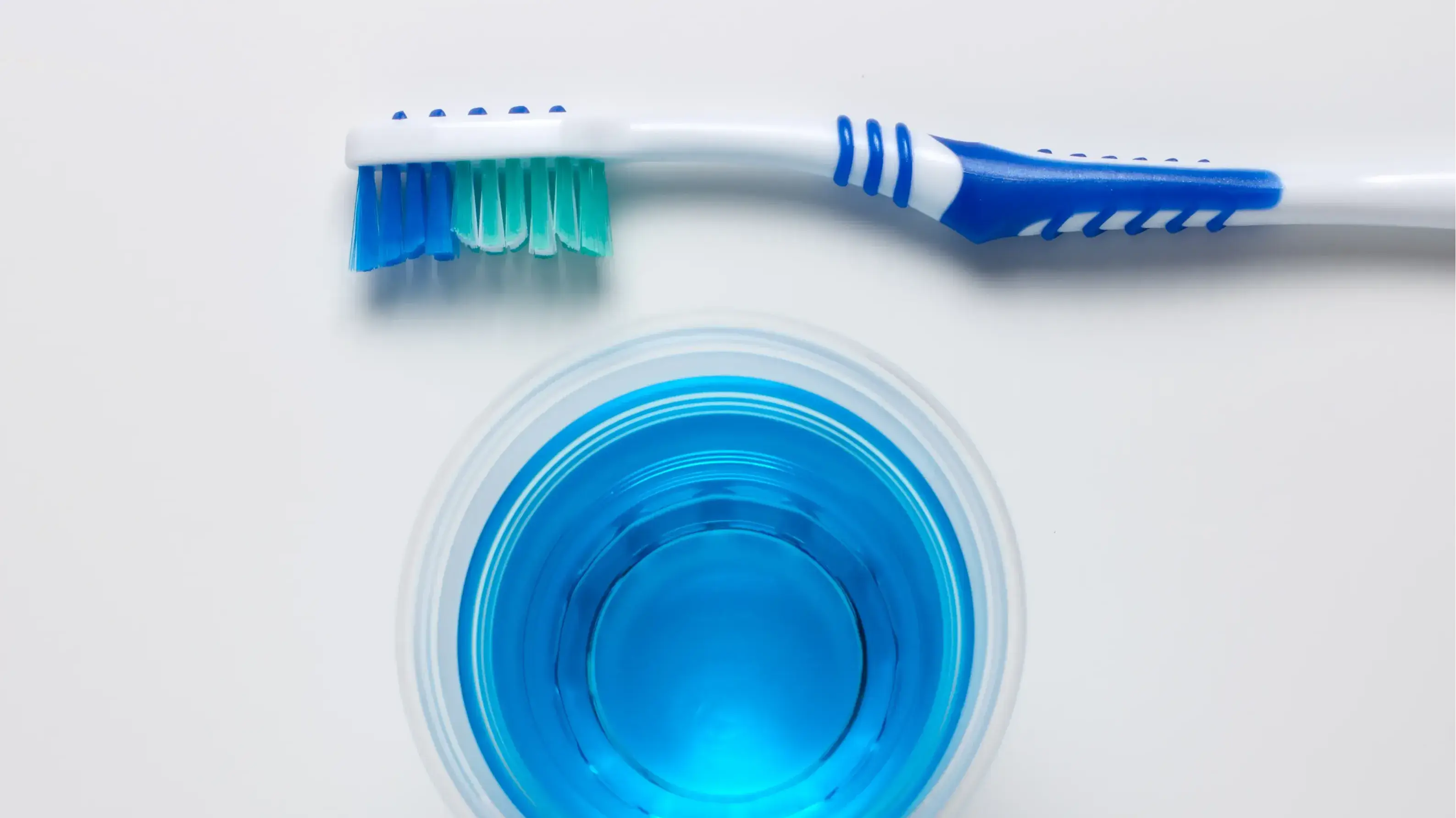 Oben und unten jeweils eine Zahnbürste und in der Mitte ein blaues Mundwasser.