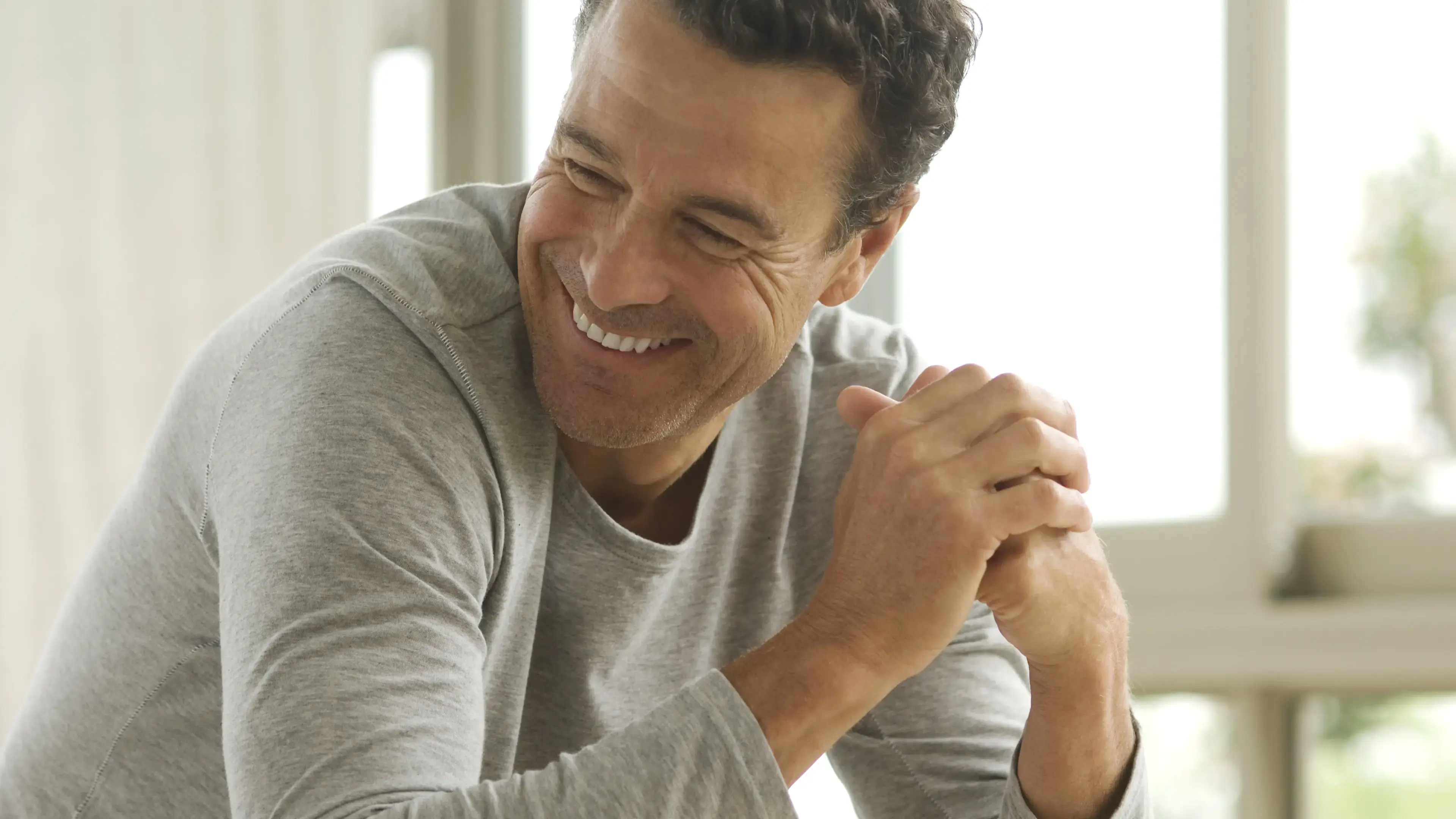 Ein lächelnder mann mittleren Alters, der seine Hände zusammen faltet.