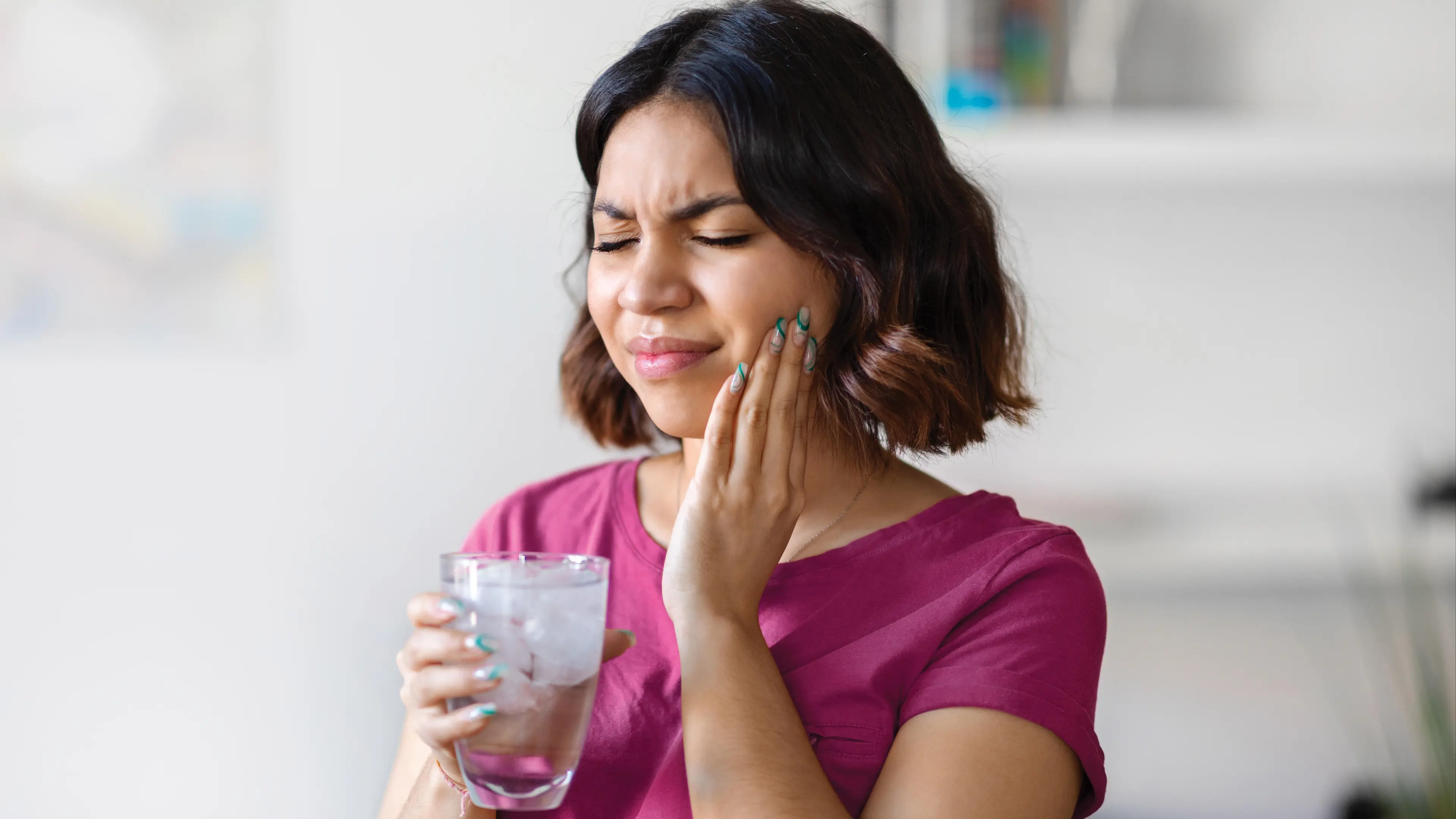 Eine Frau, die sich schmerzvoll an ihre linke Wange hält.