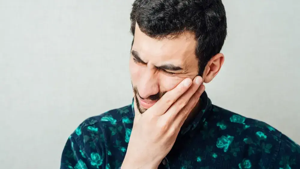 Ein Mann, dessen Gesicht schmerzverzehrt ist und sich die Hand an die linke Wange hält.