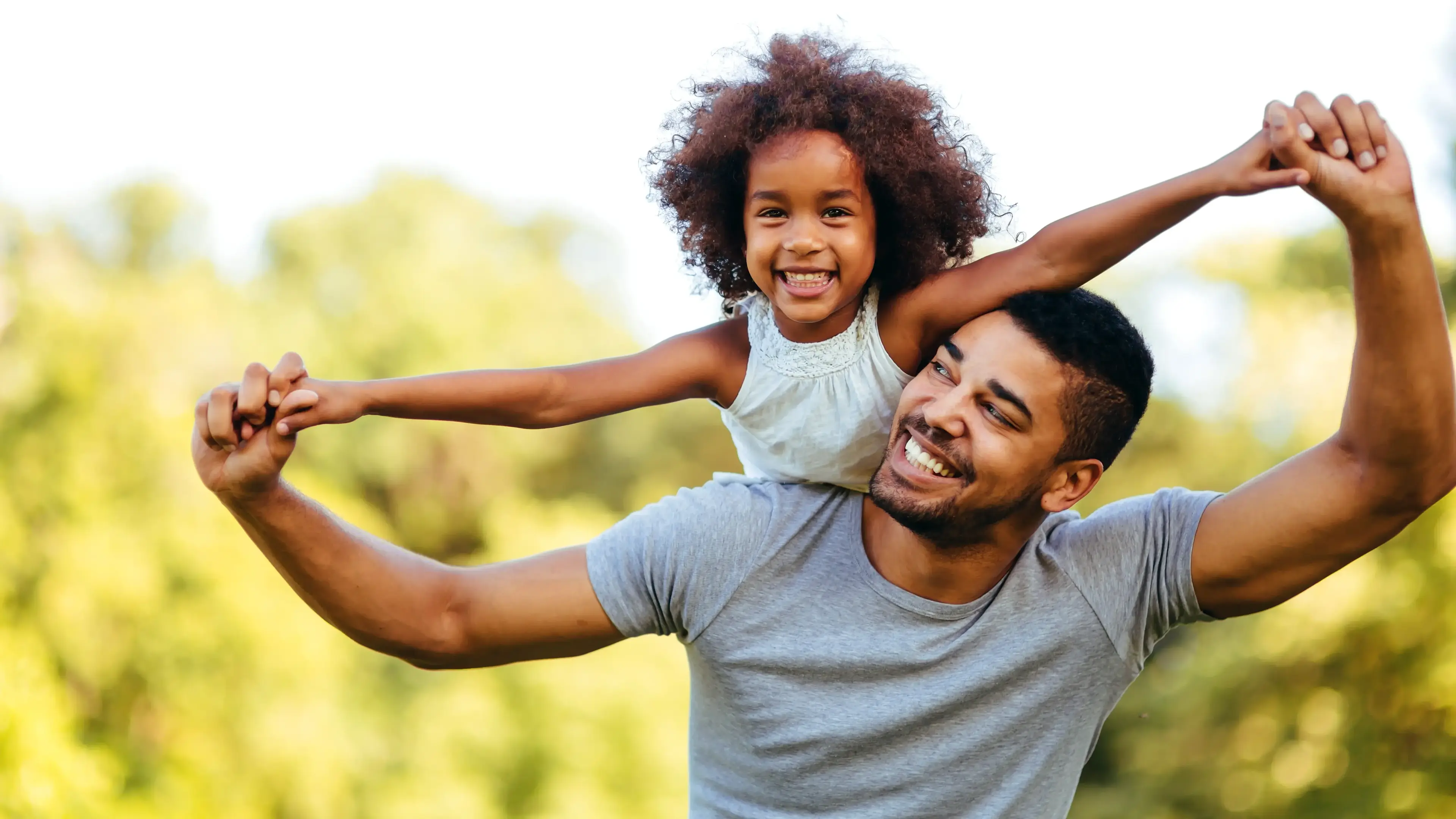 Vater trägt Tochter auf den Schultern - beide lächeln.