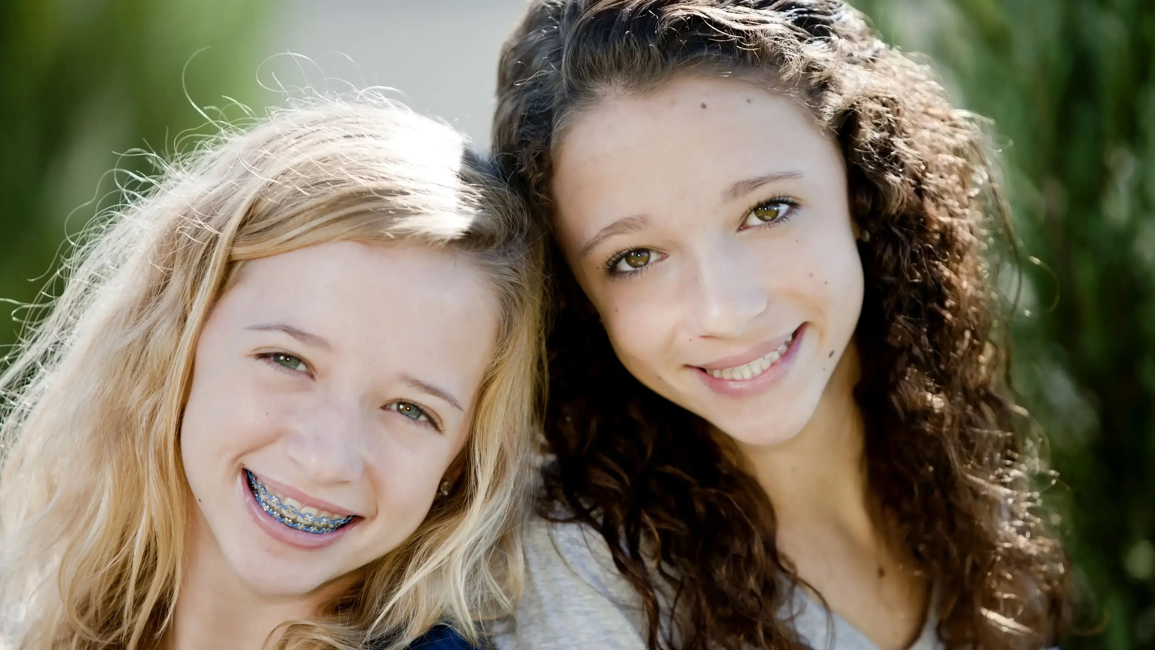 Zwei Mädchen mit Zahnspangen, die in die Kamera lächeln.