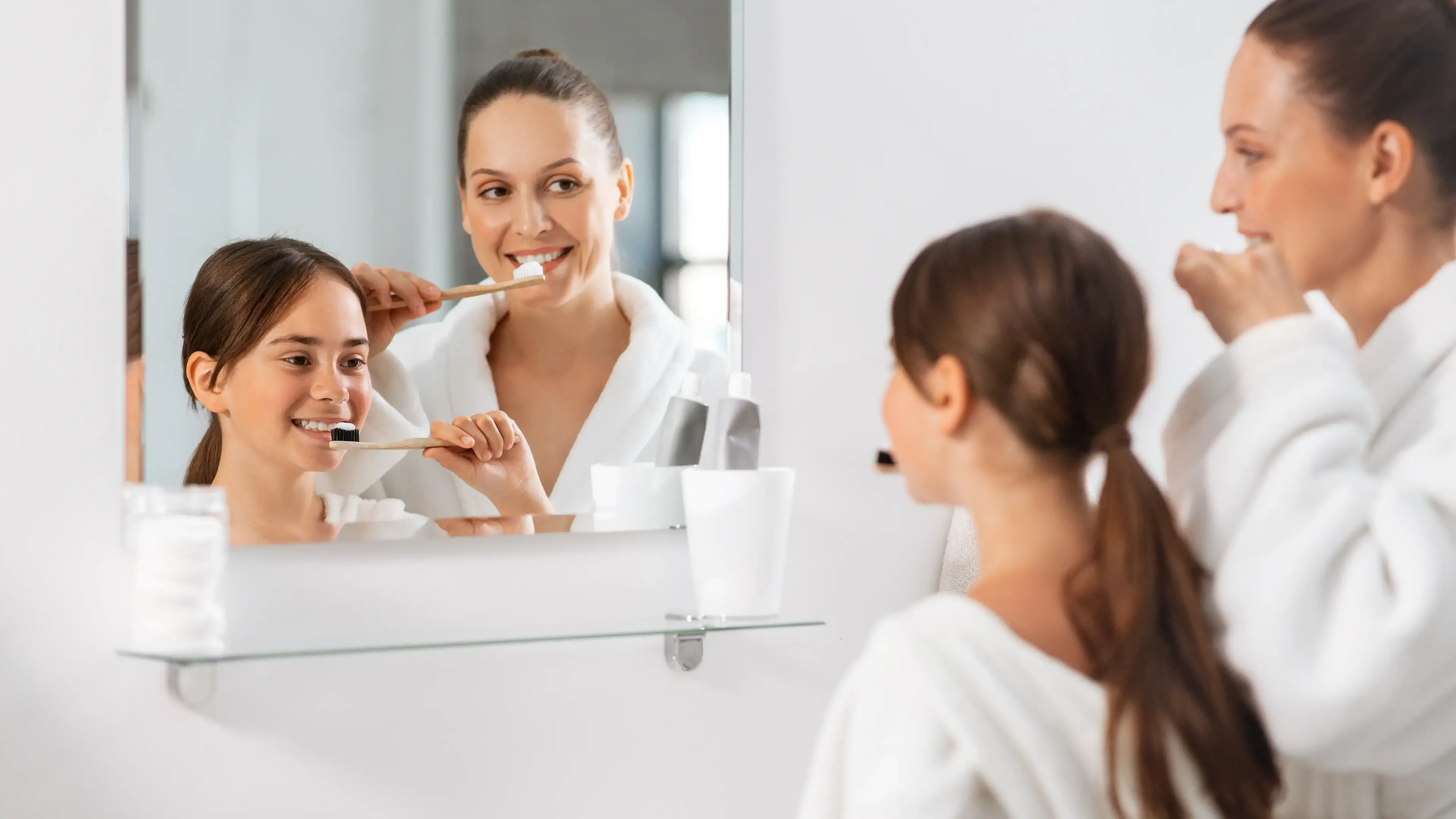 Eine Frau und Kind, die vor dem Badspiegel ihre Zähne putzen.