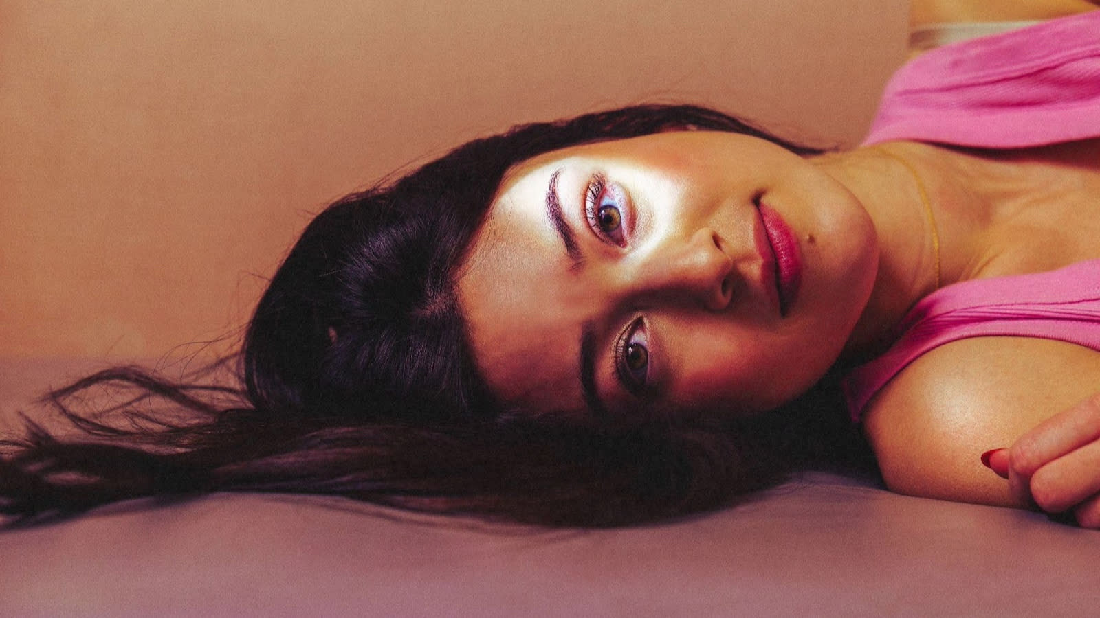 A woman lying on a pink-to-orange ombre backdrop.