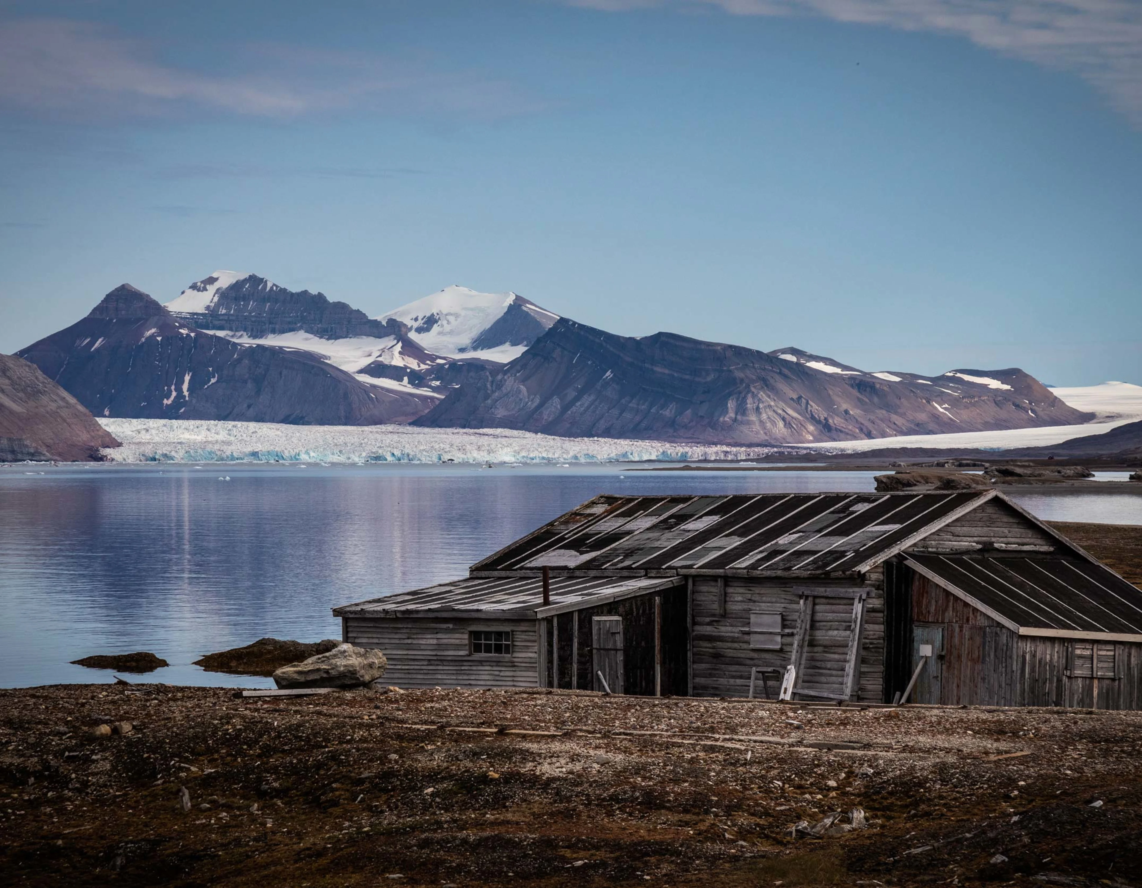 Old wooden cabin in Ny-Ålesund, sea and partly snow covered mountains in  the background.