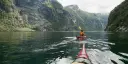 Kayaking in Geirangerfjord, people paddling kayak, mountain walls to the left and right.