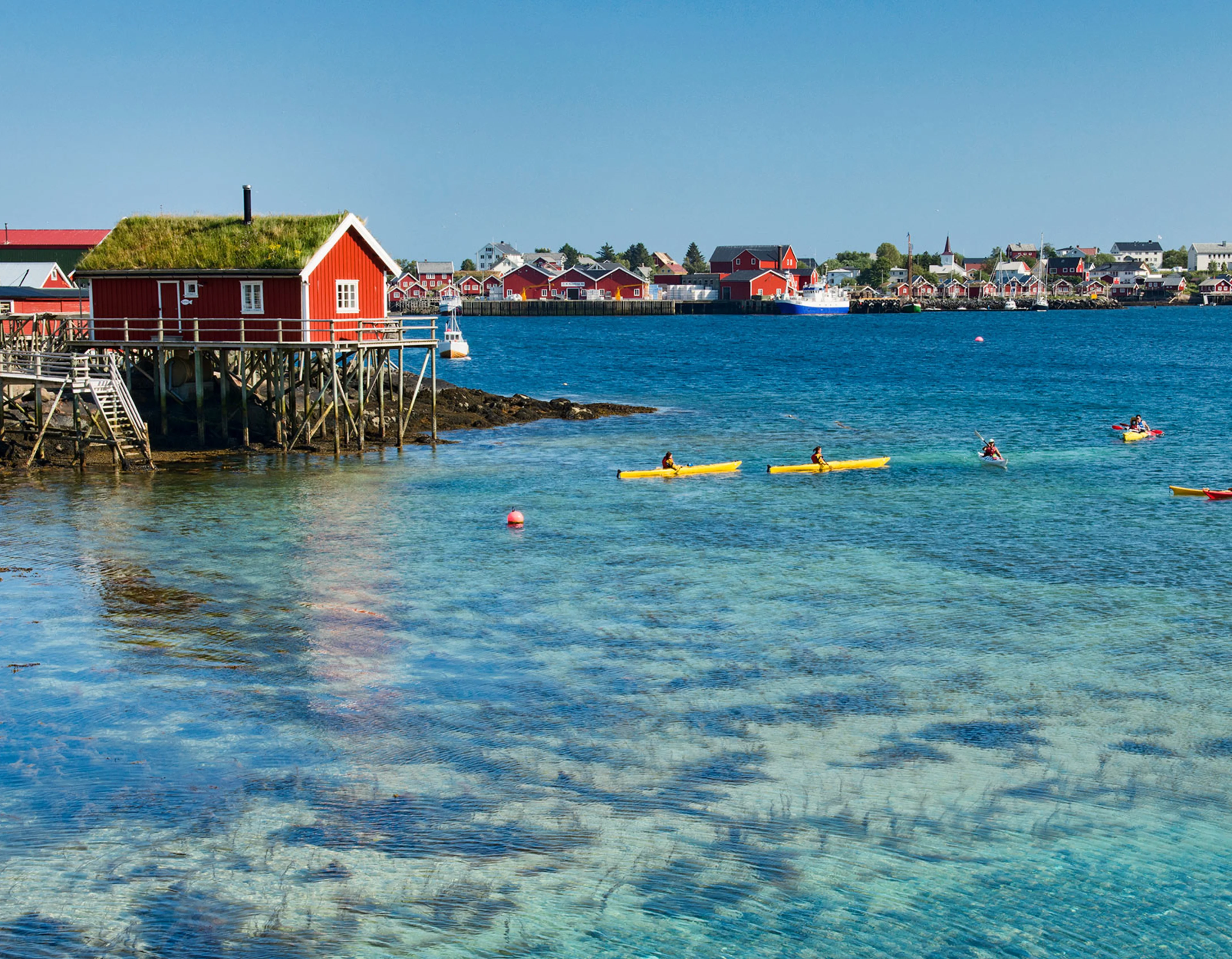 Kayaking excursion in clear turquoise waters close to red fishing huts in Reine, Lofoten
