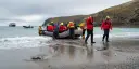 People in red jackets landing on a beach with a rib boat.