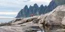 Two people in red jackets hiking on cliffs in front of the mountains on Senja.