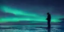 One person standing on ice, ice fishing in the dark. Northern lights in the sky.