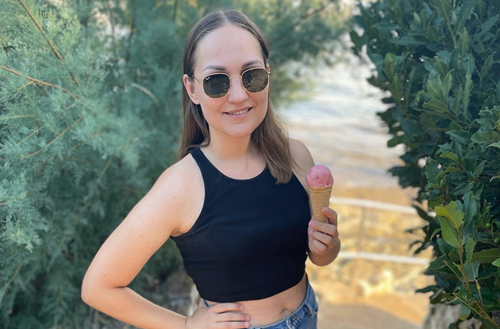 Woman with sunglasses standing in a park smiling to the camera while holding an icecream