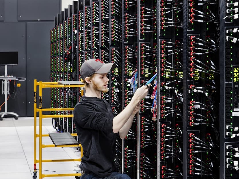 Homem branco trabalhando em um rack de servidor em um data center.
