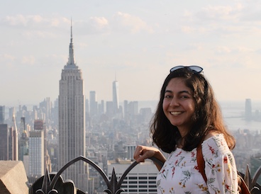 Young girl smiling at the camera, posing on a rooftop with great city view.
