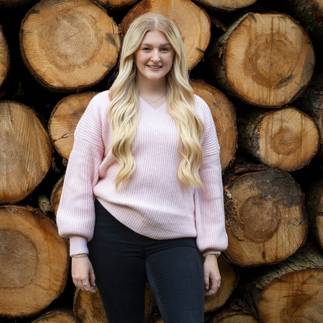 Young blonde woman smiling, tree trunks in the background.
