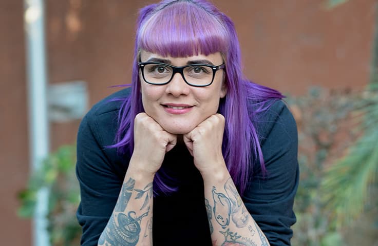 Woman with violet hair and tattoos, smiling