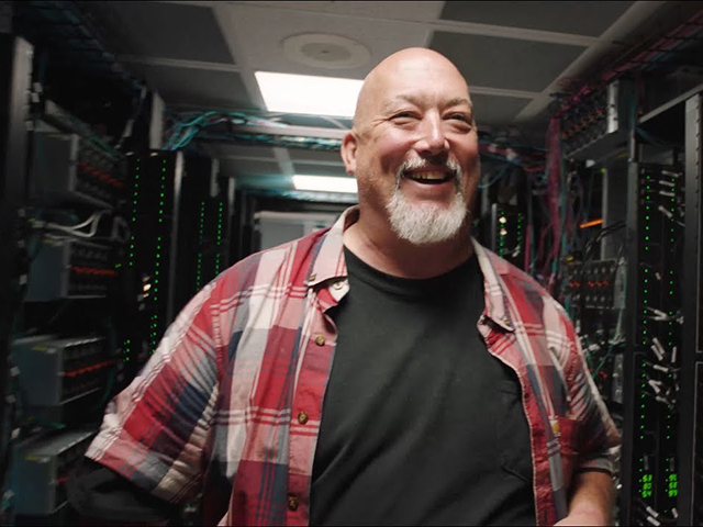 Man with white beard smiling at the camera inside a data center.