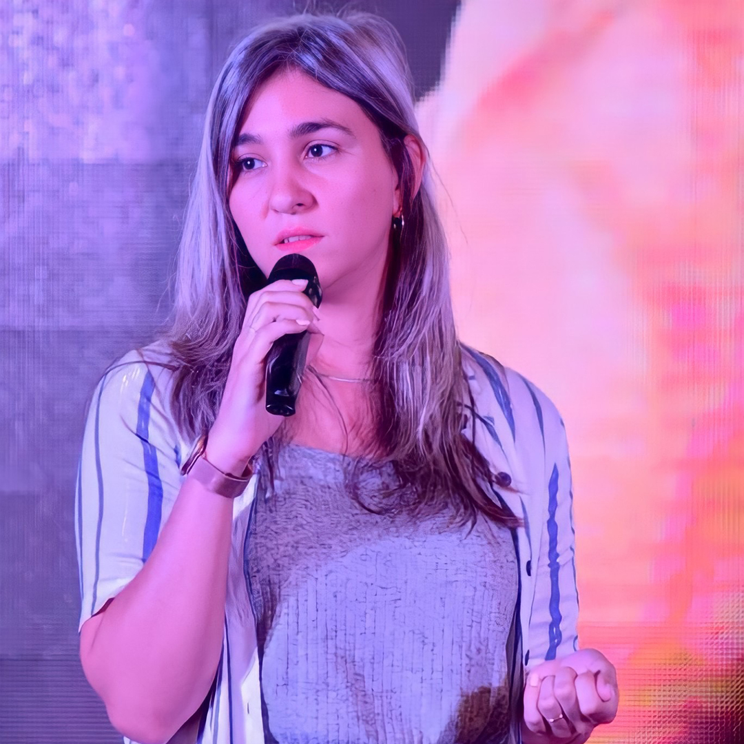 Mujer joven con cabello gris dando un discurso, contra un fondo colorido.